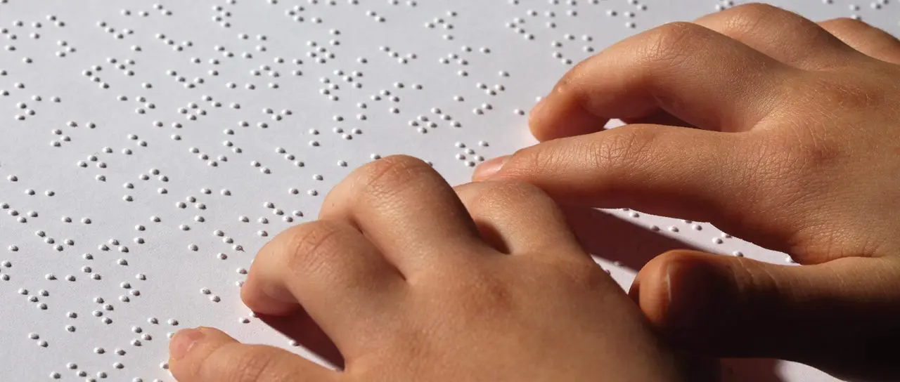 Close-up of a child's hands resting on a page of braille, fingertips touching the raised dots.