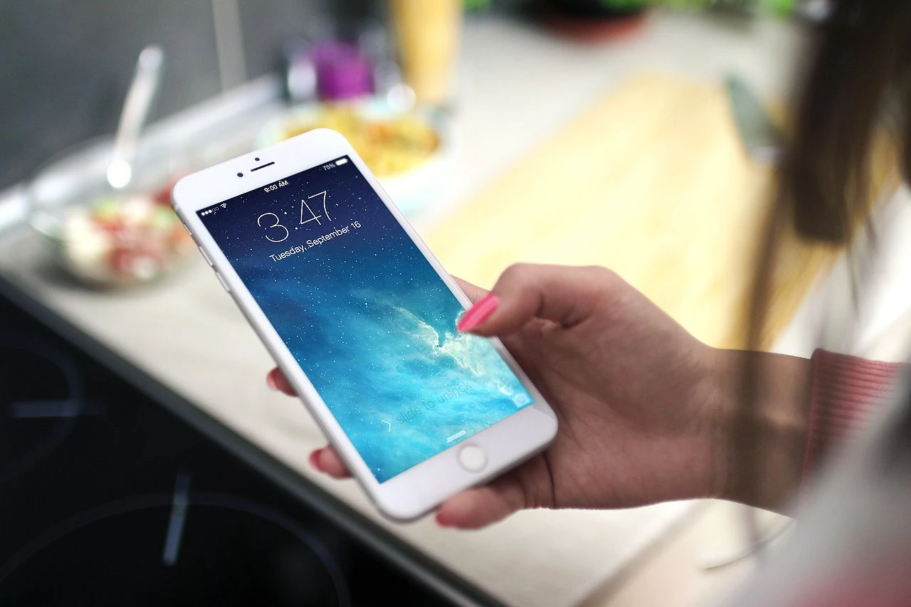A person holding a mobile phone in their hand which shows the time.