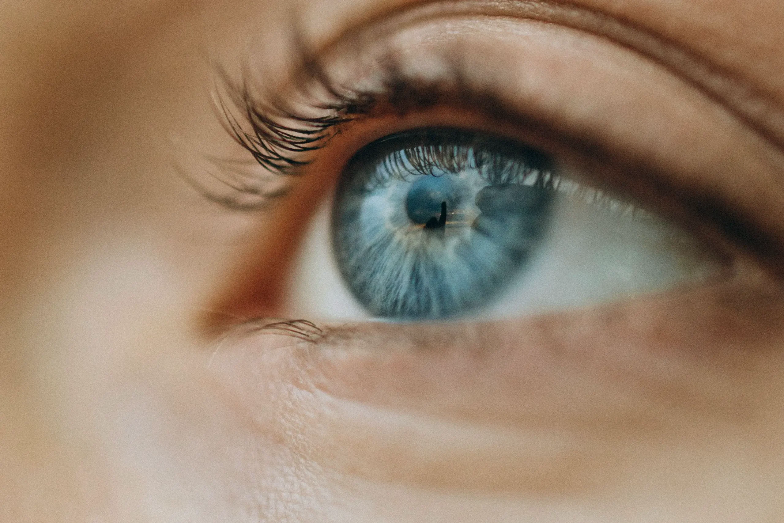 Extreme close-up of a person's blue eye, looking up and to the side, with lashes and the surrounding skin softly out of focus.