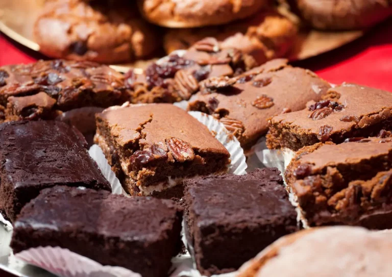 A tray of home-baked cakes, including chocolate brownies, pecan slices and cookies, on a red tablecloth.