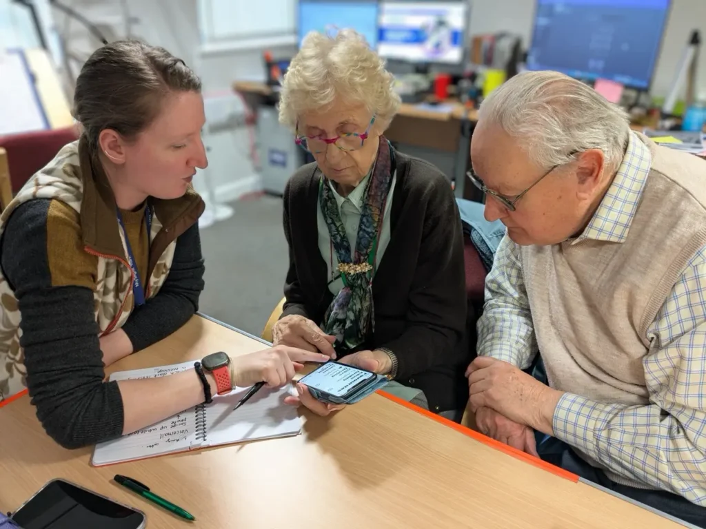 A MySight York staff member points at a smartphone screen while an older woman and man look on.