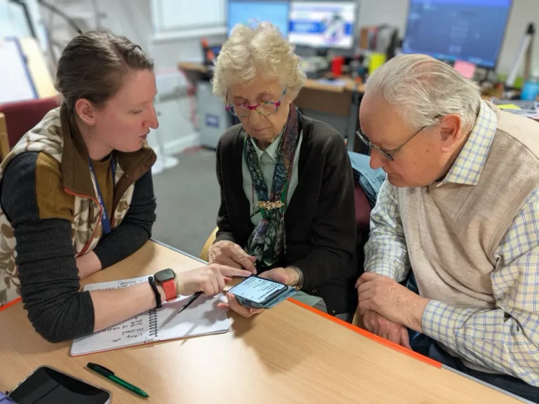 A MySight York staff member points at a smartphone screen while an older woman and man look on.