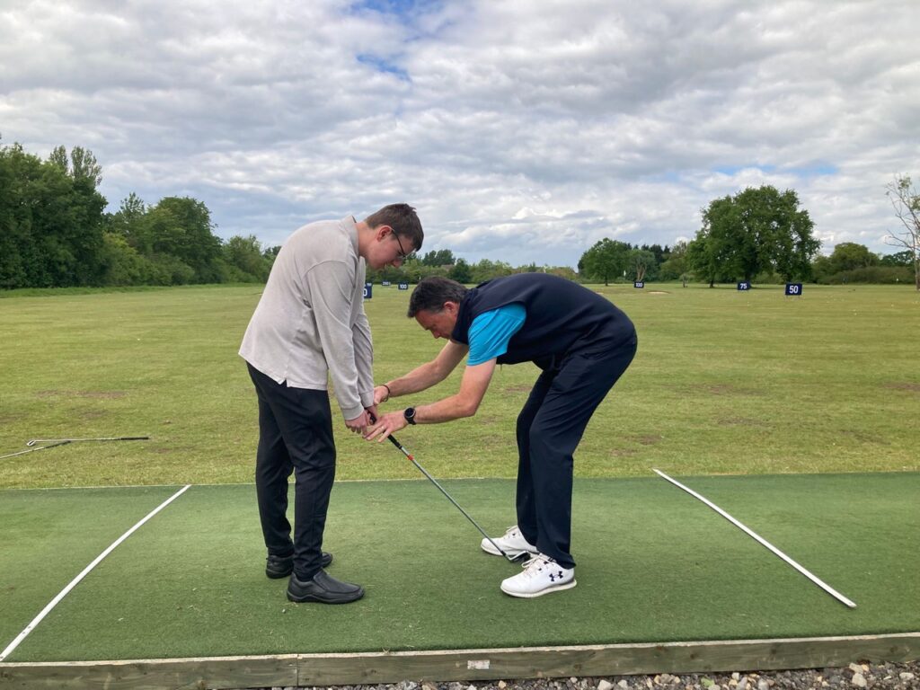 A golf coach adjusts a young man's grip on his club at a driving range.