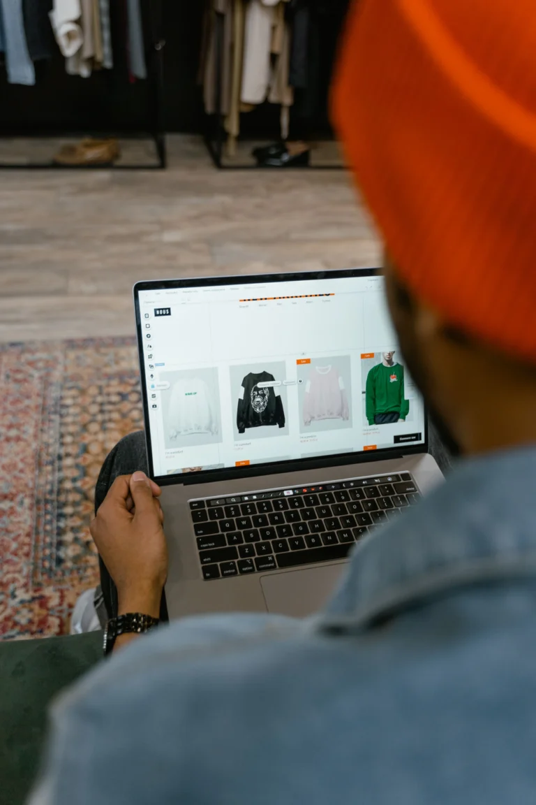 Person seated indoors using a laptop to browse an online clothing store.